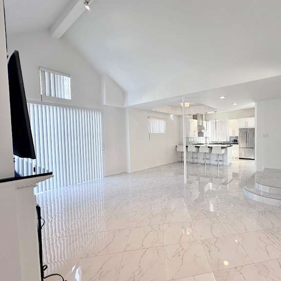 a spacious living room with a television and a dining area in the background.