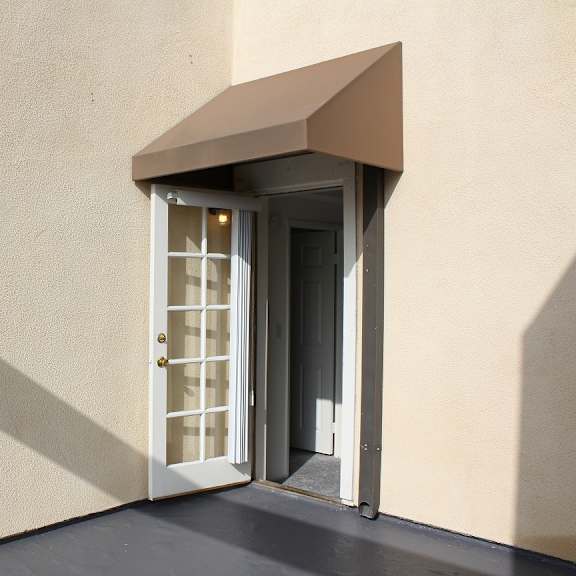 a white door with a brown awning is open to a dark interior.