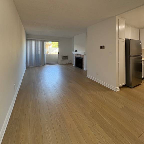 a room with wooden flooring and a refrigerator on the right side.