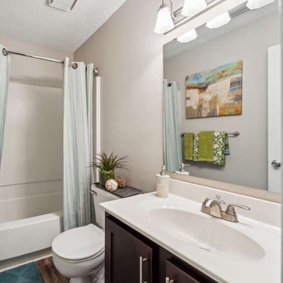 a bathroom with a white toilet, a sink, and a shower with a blue shower curtain. at the timbers apartments, virginia, 23235