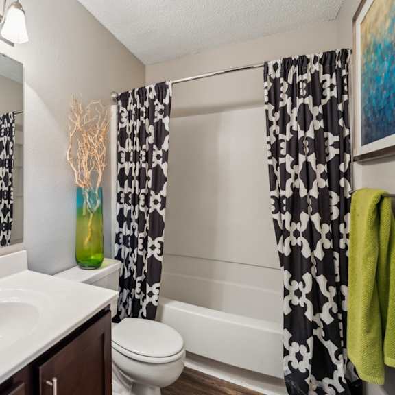 a bathroom with a white sink, toilet, and a painting on the wall. at the timbers apartments, richmond 23235