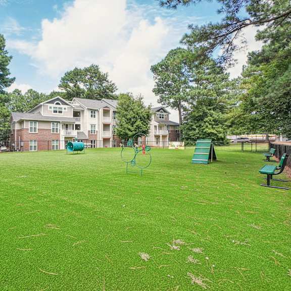 a grassy field with a playground and apartment buildings in the background at the falls apartments in raleigh nc