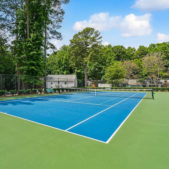 a tennis court with blue and green turf and a fence and trees at lake johnson mews, raleigh