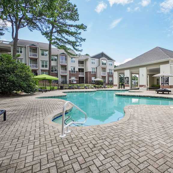 a swimming pool surrounded by a brick patio and apartment buildings at the falls apartments in raleigh nc