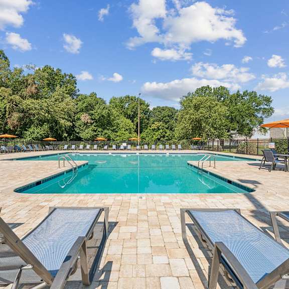 a pool surrounded by lounge chairs and umbrellas at staples mill townhomes apartments, richmond, va, 23228