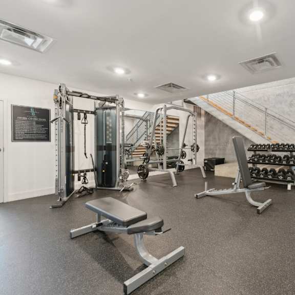 a gym with a variety of equipment including a bench, weights, and a squat rack at south falls tower apartments, richmond, va, 23224