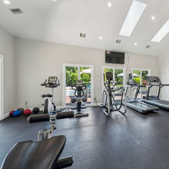 a spacious gym with a variety of equipment including treadmills, exercise bikes, and weight machines. at the timbers apartments, richmond, virginia