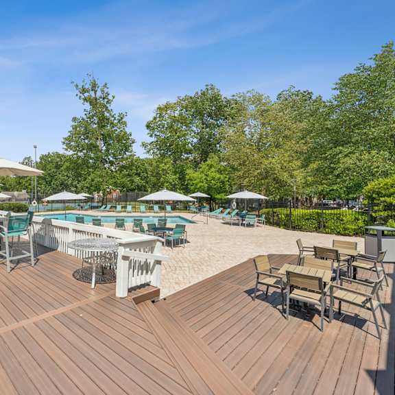 a wooden deck with chairs and umbrellas overlooking a pool. at the timbers apartments, richmond, va