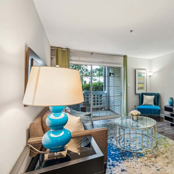 a blue lamp sits on a table in a room with a glass table and a sofa. at the timbers apartments, richmond, va