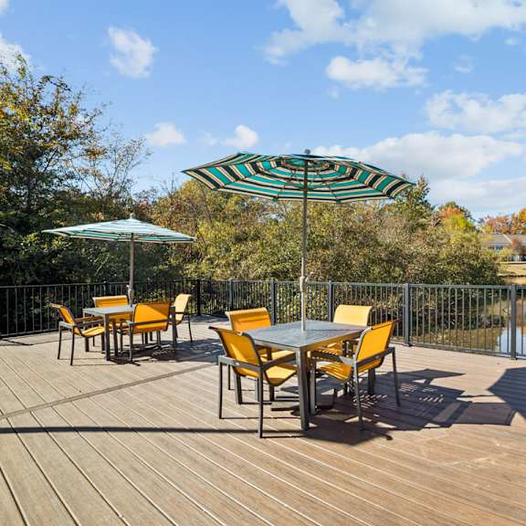 a table with chairs and an umbrella on a wooden deck overlooking a lake at lakecrest apartments, prg real estate management, greenville, sc, 29615