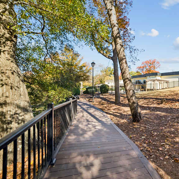a wooden walkway with a metal railing is surrounded by trees at lakecrest apartments, prg real estate management, greenville, sc, 29615