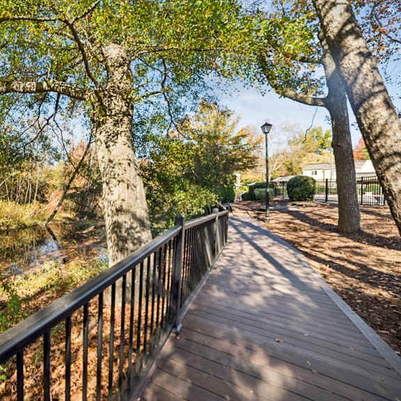 a wooden walkway with a metal railing runs through a wooded area at lakecrest apartments, prg real estate management, greenville, sc, 29615