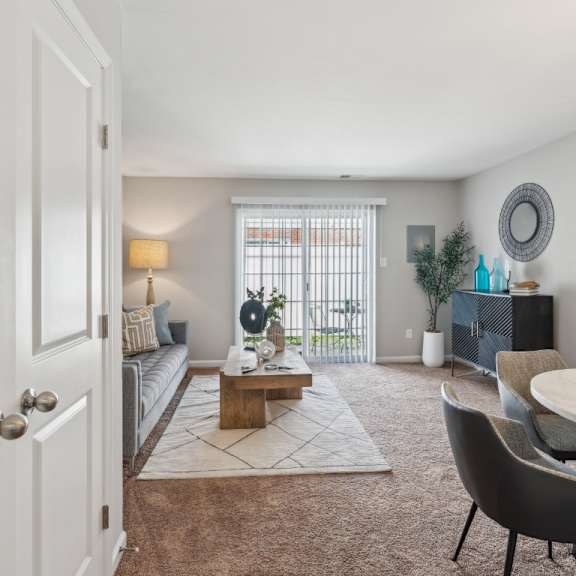 a living room with a grey couch, a wooden coffee table, a white door, a white wall, a television, a plant, and a butterfly picture at staples mill townhomes apartments, richmond 23228