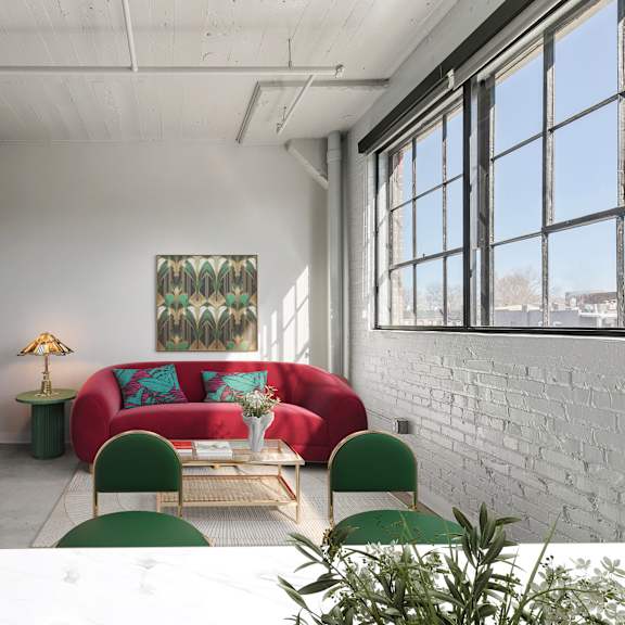 Thumbnail 2 of 7 A room with a red couch, green chairs, and a white table.