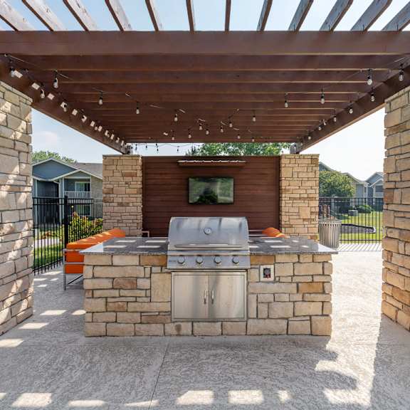 an outdoor kitchen with a grill and a tv under a pergola at the reserve at barry apartments, kansas city, missouri