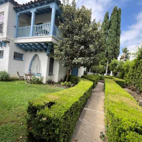 a white and blue house with a balcony and a hedge in the front yard.