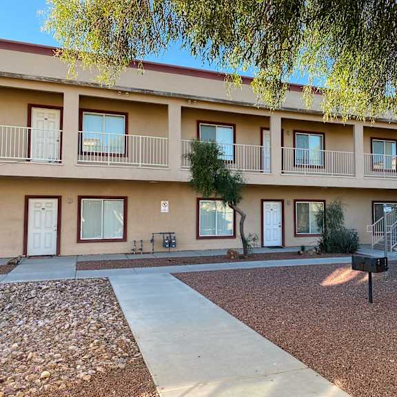 apartment complex with a tree in front and a staircase leading to the second floor.