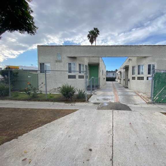 a concrete pathway leads to a building with a green fence on either side.