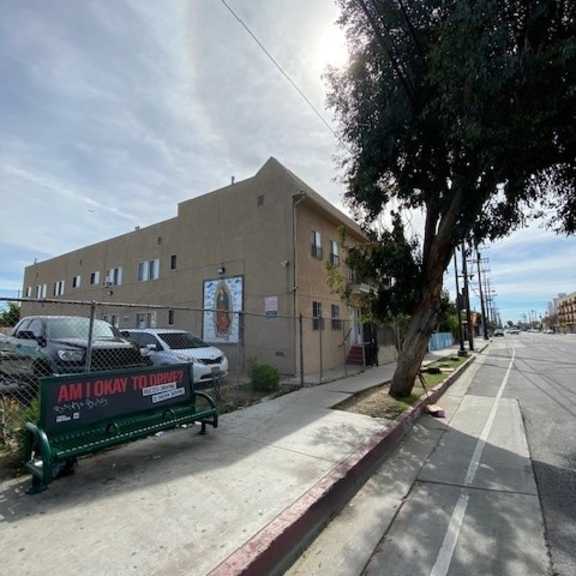 a street view with a building on the left and a bench with a sign on it.