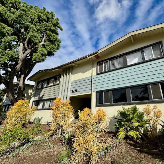 a house with a blue and beige exterior is surrounded by greenery.