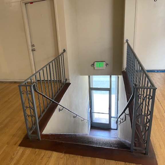 a staircase with a metal railing and wooden steps leading to a door with a green exit sign above it.