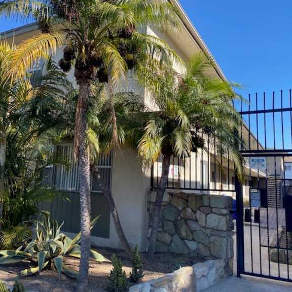 a house with a black gate and a palm tree in front.