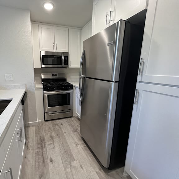 Thumbnail 3 of 7 A kitchen with a refrigerator, sink, oven, and microwave.