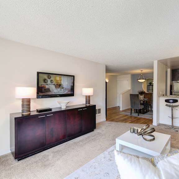 model living room with gray couch and white chair.  kitchen and counter with bar stools is visible from the living room at the retreat at walnut creek, california, 94596