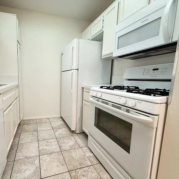 Thumbnail 14 of 39 A kitchen with white appliances and a tiled floor.