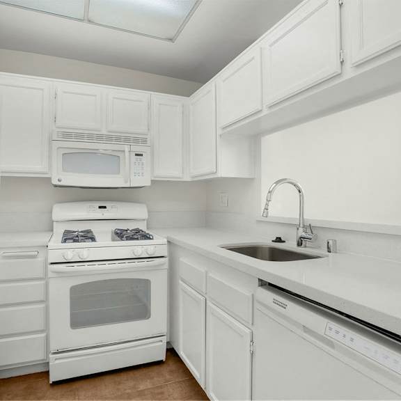 Thumbnail 3 of 13 A white kitchen with a refrigerator, microwave, oven, and sink.