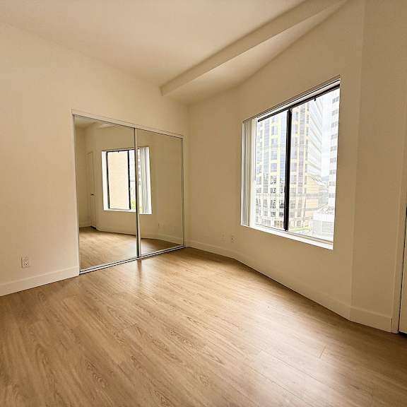 Thumbnail 9 of 26 A large empty room with a wooden floor and a large mirror on the wall.