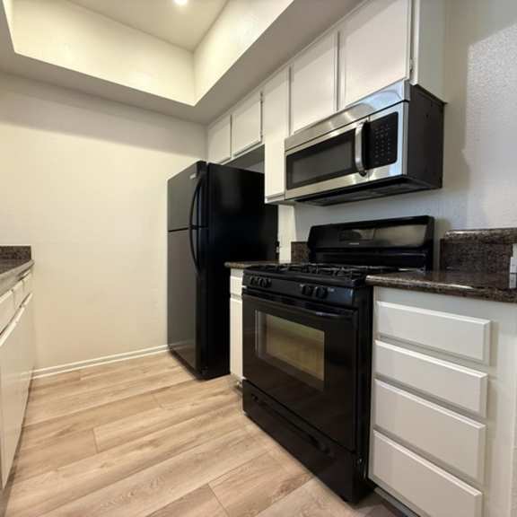 Thumbnail 4 of 26 A black refrigerator is in a kitchen with white cabinets and a black stove.