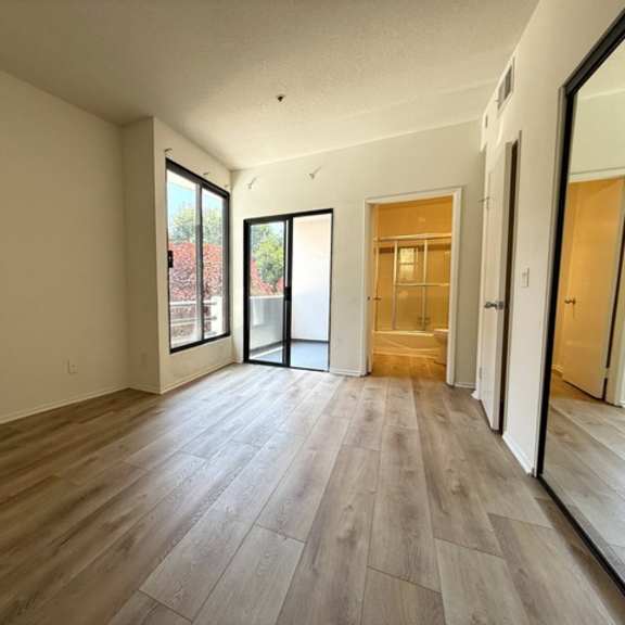 Thumbnail 8 of 26 A room with wooden flooring and a view of a red building through the glass doors.
