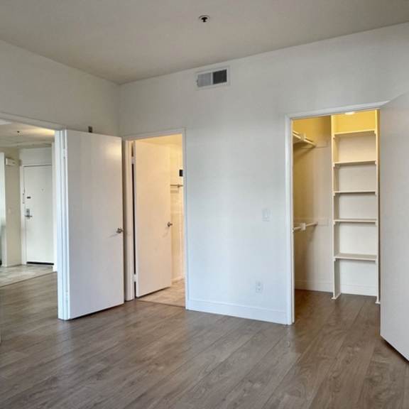 Thumbnail 10 of 11 A room with white walls and wooden flooring, with a doorway leading to another room.