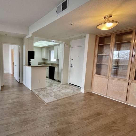 Thumbnail 5 of 11 A spacious room with wooden flooring and a kitchen area in the background.