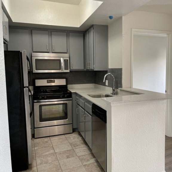 Thumbnail 6 of 11 A kitchen with a black refrigerator, stainless steel oven and microwave, and a white countertop.