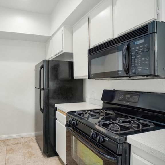 Thumbnail 4 of 17 A black refrigerator and microwave in a kitchen with white cabinets.