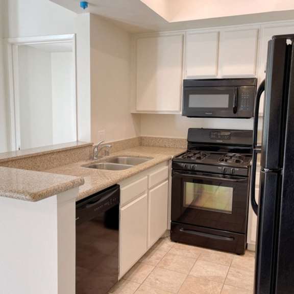 Thumbnail 10 of 18 A black refrigerator is on the right side of a kitchen with white cabinets.
