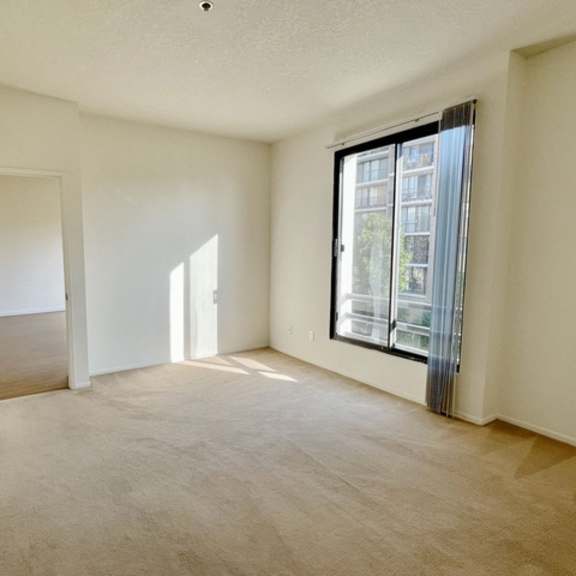 Thumbnail 7 of 18 A room with a carpeted floor, a sliding glass door, and a window letting in sunlight.