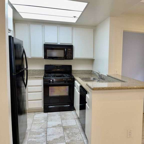 Thumbnail 7 of 8 A kitchen with black appliances and white cabinets.