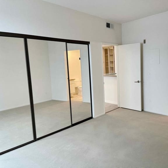 Thumbnail 5 of 8 A room with white walls and a grey floor with a glass door on the left and two white doors on the right.