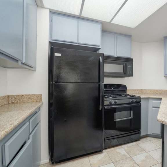 Thumbnail 6 of 11 A black refrigerator and stove in a kitchen with granite countertops.