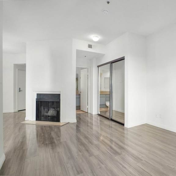 Thumbnail 7 of 11 A large empty room with a fireplace and wood flooring.