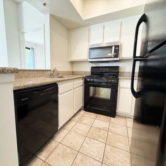 Thumbnail 6 of 18 A black refrigerator is in the corner of a kitchen with black appliances.