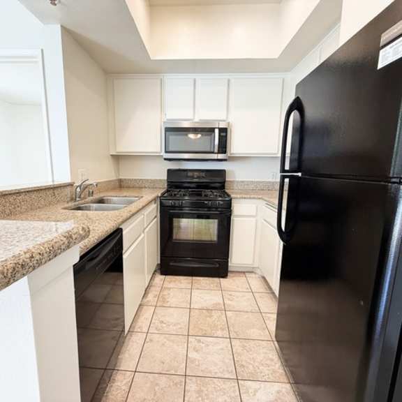 Thumbnail 3 of 18 A black refrigerator is in the corner of a kitchen.