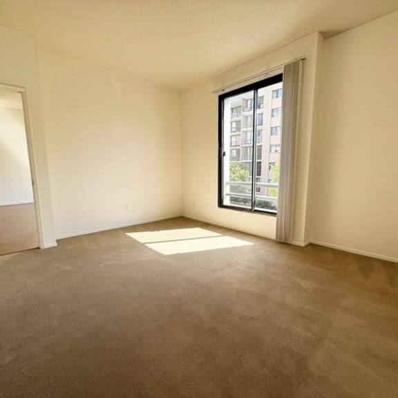 Thumbnail 11 of 18 A room with a carpeted floor and a window showing a building outside.