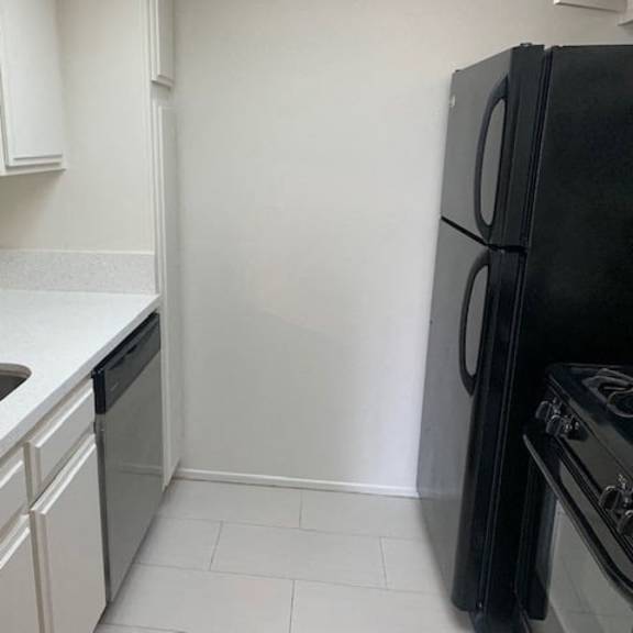Thumbnail 9 of 10 A black refrigerator sits next to a sink in a kitchen.