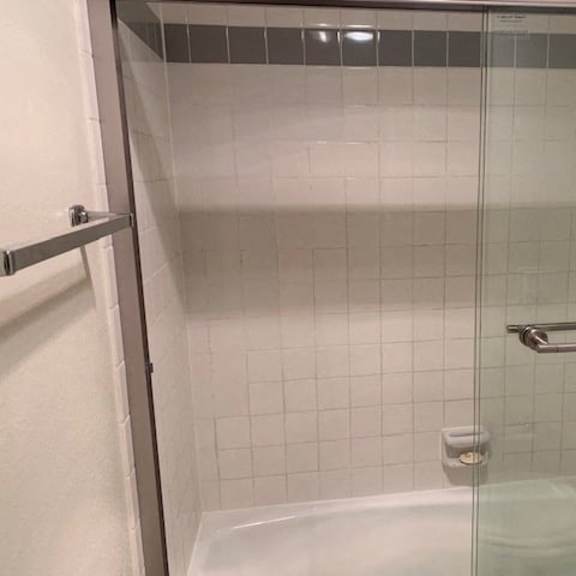 Thumbnail 10 of 10 A white tiled shower with a glass door and a silver grab bar.