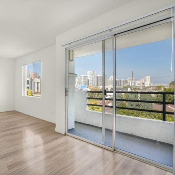 Thumbnail 3 of 28 A room with a sliding glass door leading to a balcony with a view of the city.