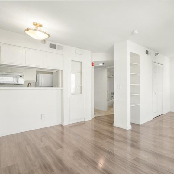 Thumbnail 10 of 28 A white room with a wooden floor and a kitchen area to the left.